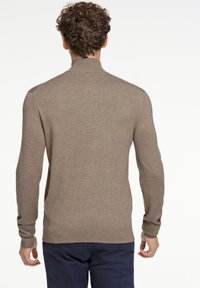 Beige stickad tröja med hög krage, långa ärmar och ribbade muddar och fåll. Slät textur med minimala sömmar för en ren finish.