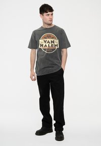 Gray cotton t-shirt with a vintage Van Halen graphic, round neck, short sleeves. Paired with black pants and black shoes.