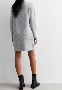 Robe tricotée grise avec des manches longues, fentes sur les côtés et une coupe ample, associée à des bottes noires avec un talon carré.