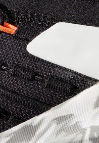 Svart teksturert stoff har en oransje aksent med en hvit plastbit integrert i designet, som skaper en funksjonell lagdelt effekt.