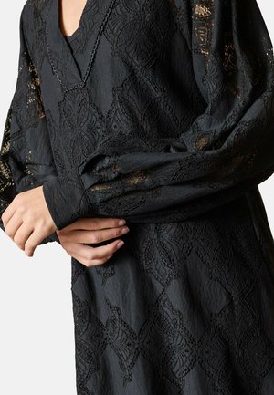 Sort kjole med intrikate blonde detaljer med blomstermønstre, lange pufærmer og V-udskæring. Tekstilet tilfører dybde.