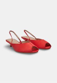 Zapatos de mujer rojos con tira trasera, punta abierta y tacón bajo, con un acabado liso, exhibidos sobre un fondo claro y sencillo.