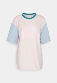 Ljusrosa oversize t-shirt med blå ärmar, med en stor, urblekt rosa adidas-logga på framsidan och en turkosa rund halsringning.