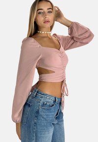 Top rosa a maniche lunghe con scollatura quadrata, centro arricciato, aperture laterali e lacci regolabili in vita, abbinato a jeans blu a vita alta.