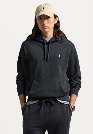 Sweatshirt cinza escuro com um bolso frontal e pequeno logotipo branco, combinado com calças a condizer e um boné bege claro. O tecido parece suave e casual.