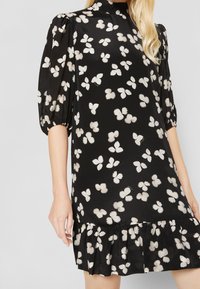 Černé šaty s nafouknutými rukávy, zdobené květinovým vzorem s krémovými motýly, s volánkovým lemem a hladkým, lehkým materiálem.