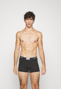 Bóxer negro elaborado en material suave con un logotipo blanco de Calvin Klein en la cintura, que presenta un ajuste ceñido y una textura lisa.