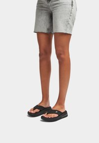 Zwarte teenslippers met een gestructureerde band en een contrasterende zool, voorzien van een gegroefde onderkant voor grip en een lichte verhoging in de hak.