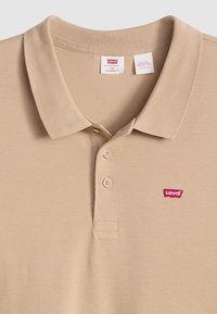 Beige pólóing texturált anyagból, három gombos nyakkivágással és egy kis piros Levi's logóval a bal mellkas felett.