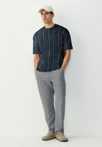 Navy short-sleeved shirt with vertical white stripes, paired with light gray loose-fitting trousers and beige slip-on shoes.