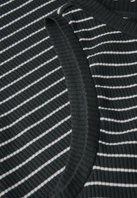 Randig ribbad tyg i svart och vitt med en strukturerad yta. Har en rund halsringning och kontrasterande kant längs halsringningen.