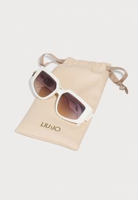 Hvide oversized solbriller med gradient linser, hvilende på en beige stofpose med snørrebånd og guld "LIU·JO" logo.