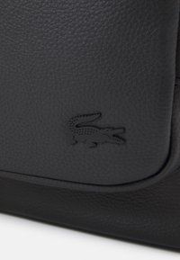 Black textured leather bag featuring a prominent embossed crocodile logo on the front, with a smooth, curved flap design.