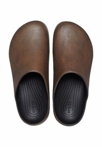 Zoccoli marroni slip-on con una tomaia sintetica testurizzata e un interno nero liscio, dotati di una soletta sagomata e un logo discreto.