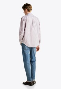 Camisa de botones a rayas con líneas rojas y azules, de manga larga y dobladillo curvado. Llevada con jeans azul claro y zapatos marrones.
