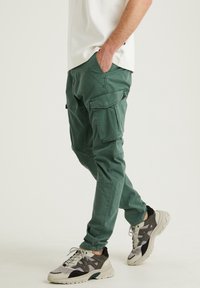 Gröna cargobyxor i bomull, med flera fickor, avslappnad passform och en mjuk textur, i kombination med moderna sneakers.
