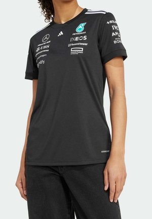 Musta Mercedes-AMG Petronas -kilpailutiimin paita, jossa on sponsoreiden logot, päällä kiharatukkainen henkilö, yhdistetty mustiin housuihin.