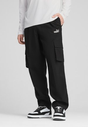 Sorte cargobukser lavet af letvægtsstof. Funktioner inkluderer sidelommer, en afslappet pasform og et hvidt logo på fronten. Kombineret med sorte og hvide sneakers.
