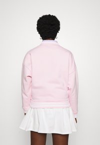 Sudadera rosa claro con cuello y puños acanalados, combinada con una falda blanca de campana, vista desde atrás. Textura suave evidente.