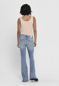 Pale pink fitted tank top paired with light blue flared jeans. The jeans feature a faded finish, back pockets, and a textured waistband.