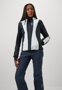 Black and light blue waterproof jacket with a zip front, features contrasting panels and a hood, paired with navy pants.