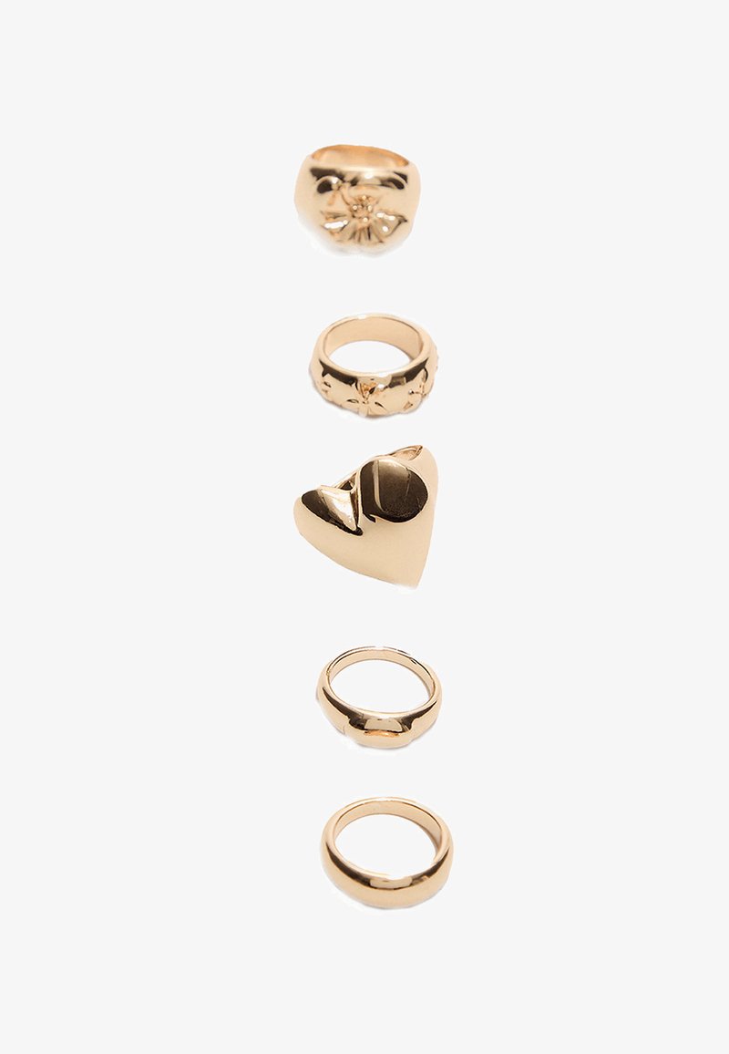 Fem guldfarvede ringe arrangeret vertikalt: en med blomsterdetaljer, en hjerteformet, og tre glatte ringe i varierende bredder.