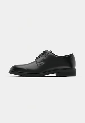 Zapato negro de cuero con cordones, punta redonda, suela de goma plana y detalles de costura sutiles. Textura suave con un diseño minimalista.