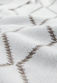 Gewebter Stoff mit einem weißen Grund und braunen Zickzackmustern. Glatte Textur mit einem feinen Strickdesign und leichtem Glanz.