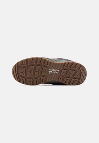 Czarna podeszwa buta trekkingowego z teksturowaną brązową gumową podeszwą z geometrycznymi wzorami dla lepszej przyczepności. Widoczne logo "Jack Wolfskin".
