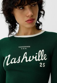 Zelena majica s dugim rukavima i bijelim rebrastim ovratnikom, sa natpisom "Nashville" ispisanim kurzivom i "Tennessee, U.S.A." ispisanim iznad u bijeloj boji. Broj "25" u bijeloj boji.
