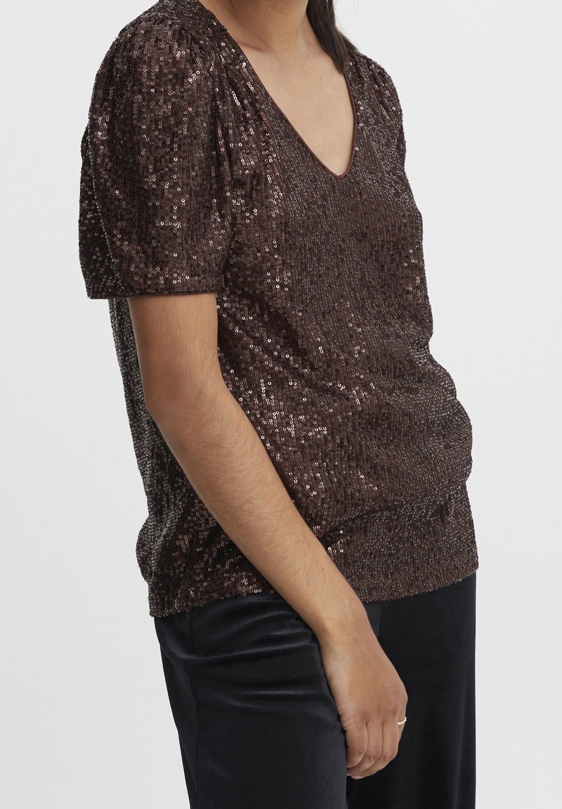 Brun paljettröja med korta puffärmar och V-ringning. Slät textur med en figurnära siluett. Matchad med svarta byxor.
