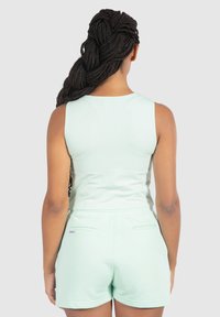 Conjunto de top sin mangas y pantalones cortos en verde menta, hecho de tela suave. Cuenta con un escote redondeado, diseño sin mangas y bolsillos traseros en los pantalones cortos.