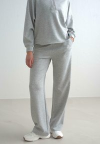 Grå fleece sweatshirt med halvlukning og broderet logo, parret med matchende vide bukser. Hvide sportsko fuldender looket.