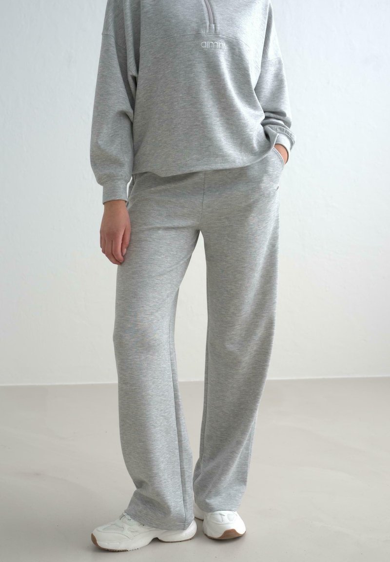 Grå fleece sweatshirt med halvlukning og broderet logo, parret med matchende vide bukser. Hvide sportsko fuldender looket.