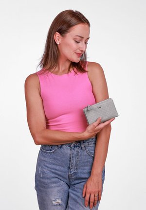 Gray quilted wallet held in hand, featuring a zipper closure and subtle logo. Model wears a pink tank top and high-waisted denim jeans.