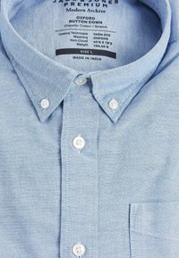 Camisa de botón Oxford azul claro hecha de algodón orgánico. Presenta un cuello estándar, botones blancos y un bolsillo. Talla L etiquetada.