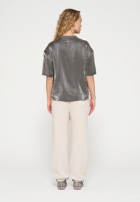 Silberner, metallischer Kurzarm-Top kombiniert mit hellbeigen, lässigen Hose im lockeren Schnitt, die eine weiche Textur und ein gemütliches Design aufweist. Schlichte Rückansicht.