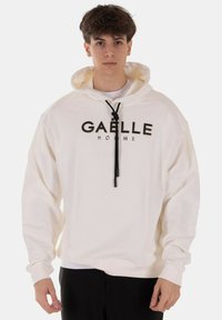 Felpa color crema in cotone con coulisse visibile e scritta nera "GAELLE HOMME" sul fronte. Maniche lunghe, vestibilità rilassata.
