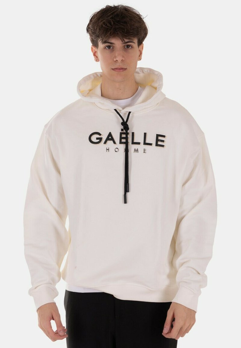 Felpa color crema in cotone con coulisse visibile e scritta nera "GAELLE HOMME" sul fronte. Maniche lunghe, vestibilità rilassata.