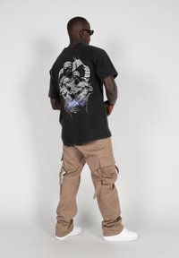 Sort grafisk t-shirt med et detaljeret design på ryggen, parret med beige cargo bukser med flere lommer og hvide sneakers.