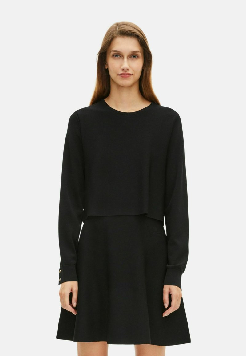 Zwarte lange mouwen jurk met een cropped top, uitlopende rok en gouden knopenaccenten op de mouwen, met een gladde textuur.