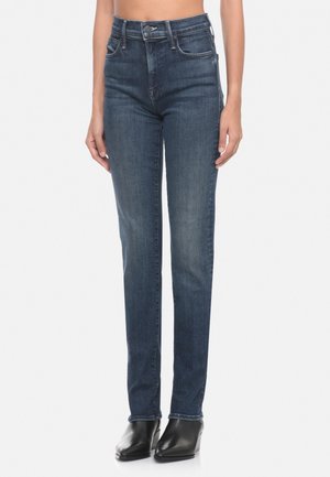 Jeans slim-fit a vita alta di colore blu scuro con una texture liscia, cinque tasche e cuciture decorative sul retro. Stivaletti neri con tacco.