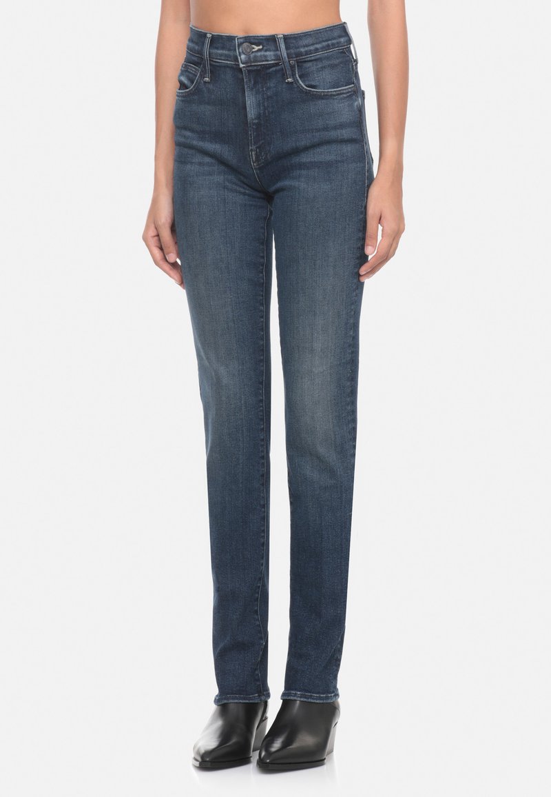 Jeans slim-fit a vita alta di colore blu scuro con una texture liscia, cinque tasche e cuciture decorative sul retro. Stivaletti neri con tacco.