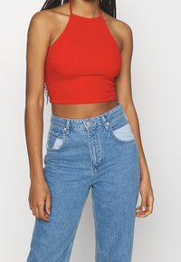 Top corto a halter rosso a coste abbinato a jeans in denim chiaro a vita alta con tasche applicate a contrasto. Texture liscia.
