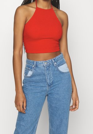 Rød ribbet halterneck crop top parret med lyseblå højtaljede denim-jeans med kontrasterende lapper på lommerne. Glat tekstur.