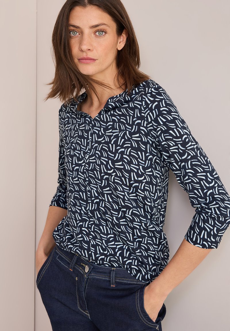 Blusa blu navy con motivo astratto bianco, scollatura tonda e maniche a tre quarti. Abbinate a jeans scuri.