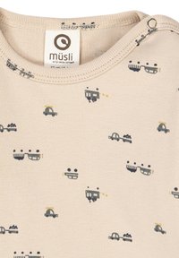 Beige cotton top with a ribbed texture, featuring colorful printed patterns of vehicles, including trucks and tractors, and a tag at the collar.