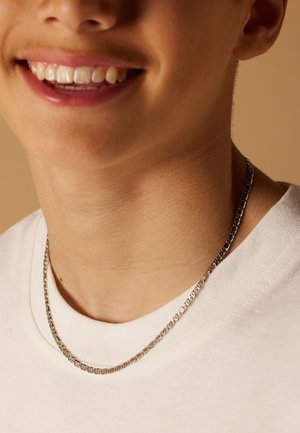 Zilveren ketting met onderling verbonden schakelstukken die rust op een lichtgekleurde T-shirt, wat de gladde textuur en gepolijste afwerking benadrukt.