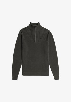 Donkergroene gebreide trui met een hoge kraag en een halve ritssluiting. Heeft een geribbelde textuur en een klein logoplaatje op de borst.