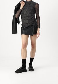 Top a maniche lunghe in rete nera con stampa leopardata, abbinato a una mini gonna in ecopelle. Scarpe nere e calzini completano il look.